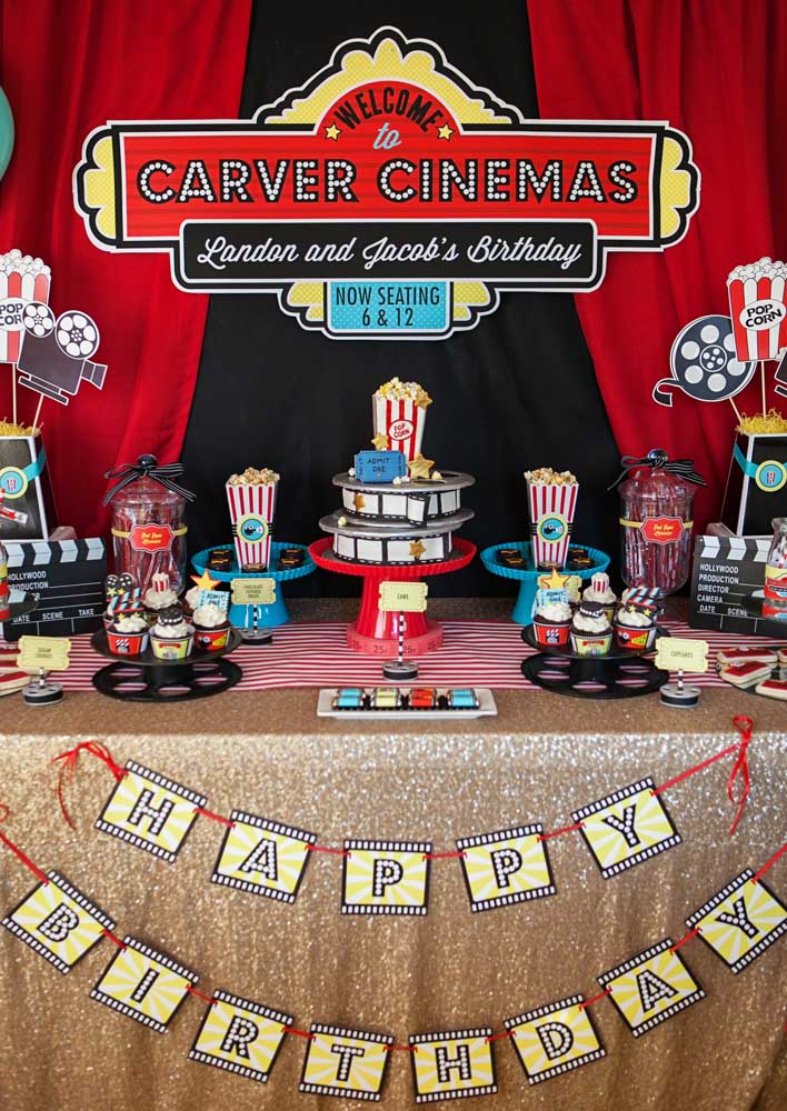 Cinema party decorated in shades of black, red and yellow. On the cake table, bags of popcorn and cupcakes